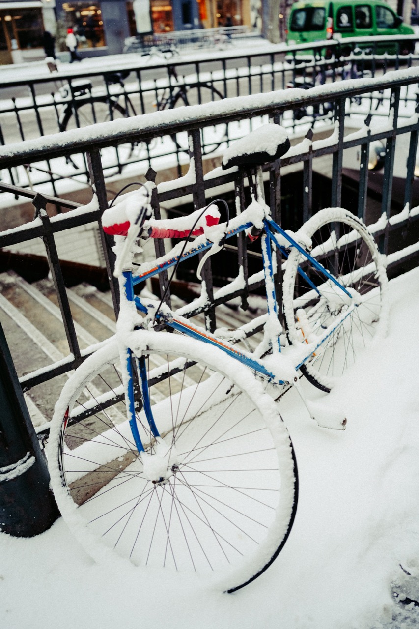 Snow-covered road bike chained to a metro railing