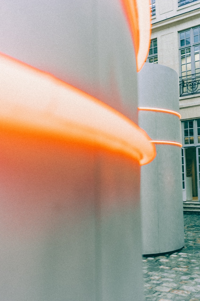 Orange glowing cylinder installation in courtyard