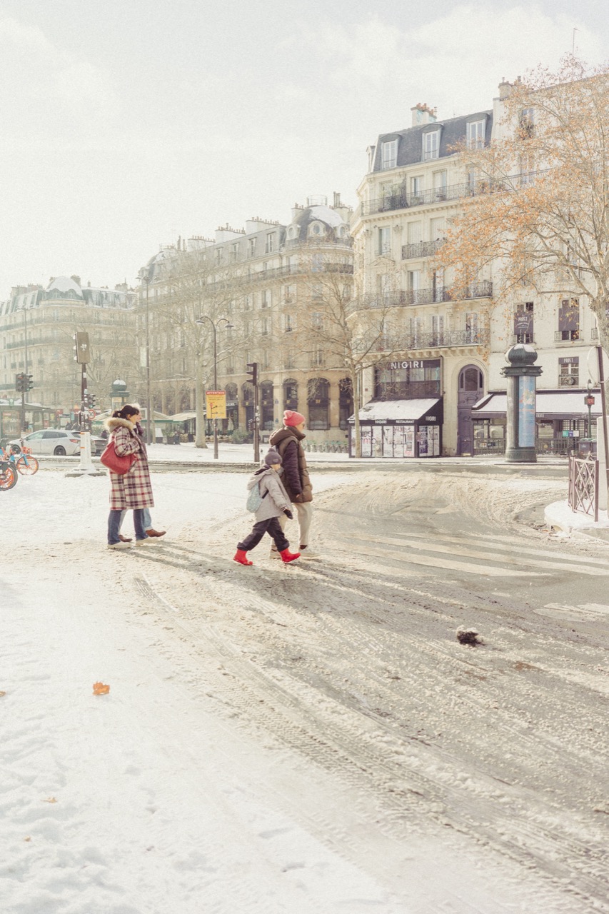 Parent and child crossing a snowy street, Haussmann buildings behind
