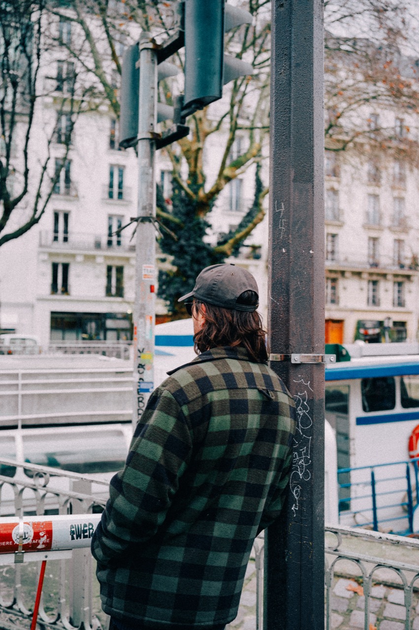 Man in check shirt leaning against a signal pole by the canal